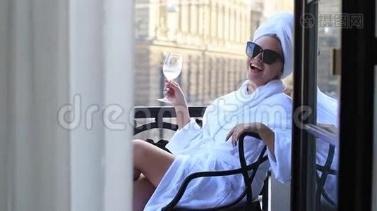 美丽的女孩在度假，带着一杯香槟坐在阳台上，看着框架视频