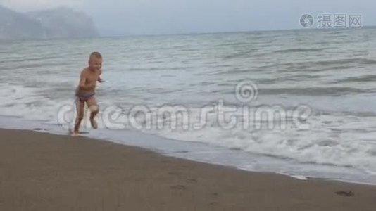 晒黑的男孩在金色的沙滩上沿着海岸奔跑。 慢动作视频