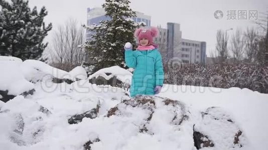 一个小女孩在冬天的公园玩雪球，唱歌，欢乐的打击。视频