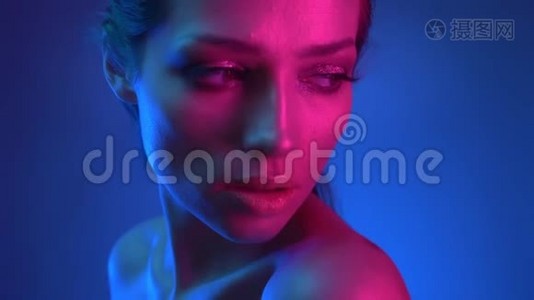 特写镜头在模特的轮廓与闪光的化妆，蓝色和粉红色的霓虹灯在肩膀上观看镜头视频