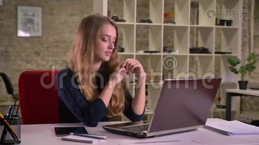 一幅漂亮的白种人金发女商人在办公室的笔记本电脑前慢慢跳舞的肖像。视频