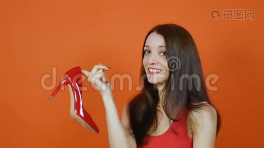 一个漂亮的棕色头发的年轻女孩检查一双红色的鞋子。 情感。 一幅橙色画室里的画视频