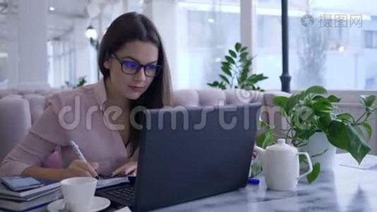 现代教育技术，成功的年轻女性在工作期间在智能手机上用笔记本电脑和视频