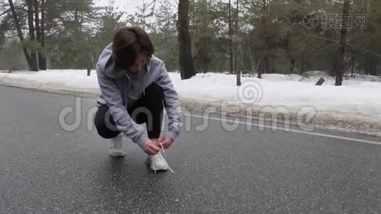 年轻漂亮的白人女孩在冬天在雪地公园跑步前系鞋带视频