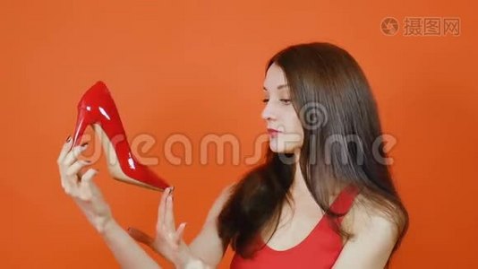 一个漂亮的棕色头发的年轻女孩检查一双红色的鞋子。 情感。 一幅橙色画室里的画视频
