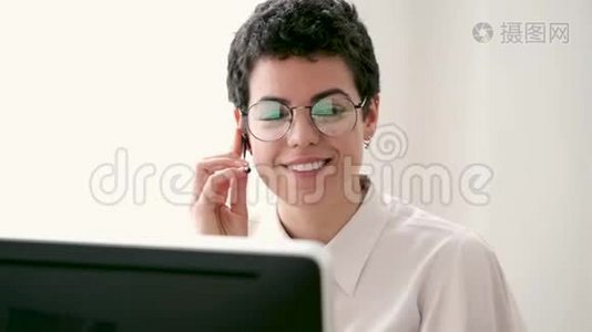 微笑的年轻商务女性使用她的自由手打电话，而她的电脑在办公室工作。视频
