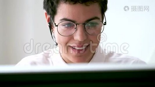 微笑的年轻商务女性使用她的自由手打电话，而她的电脑在办公室工作。视频