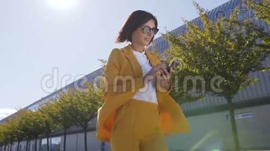 戴墨镜的年轻女商人在城市街头散步，在外面使用现代智能手机的肖像视频
