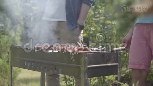 在花园里做烧烤的不可辨认的男人的特写镜头。 夏日休闲。 朋友们在烤架上煮肉。视频