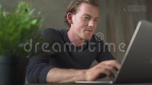 微笑的商务年轻人坐在电脑前，在笔记本电脑上打字。 帅哥商人发短信说视频