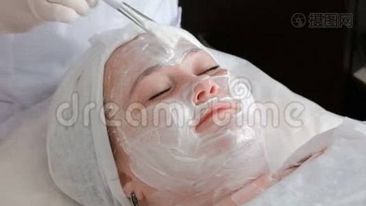 一位职业美容师戴着白手套，用一种滋养霜涂抹在女性脸上视频