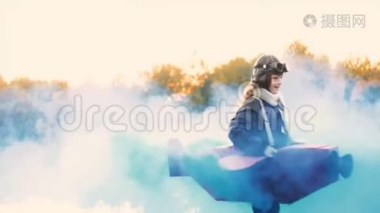 小快乐飞行员女孩旋转在有趣的纸板飞机与蓝色烟雾假装是一个飞行员慢动作。视频