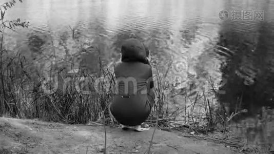 冻僵的女孩从寒冷中颤抖，坐在河岸上。 悲伤，戏剧。 单色视频。视频