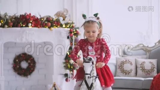 一个小女孩正在荡秋千，坐在一个有圣诞装饰和装饰圣诞树的房间里的玩具马上。视频