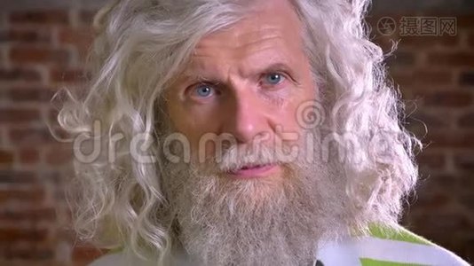 一幅老人在镜头前特写镜头的肖像，长着令人敬畏的胡须和白发，砖背景，站立视频