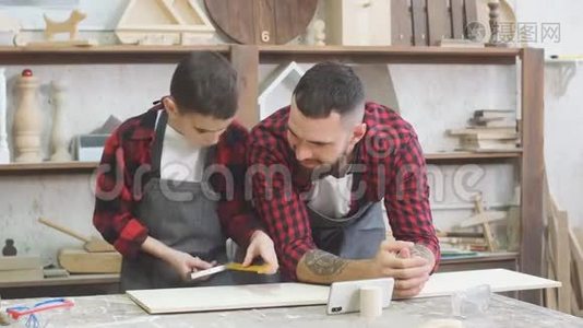 小男孩帮助他的木匠父亲测量车间里的木板。视频