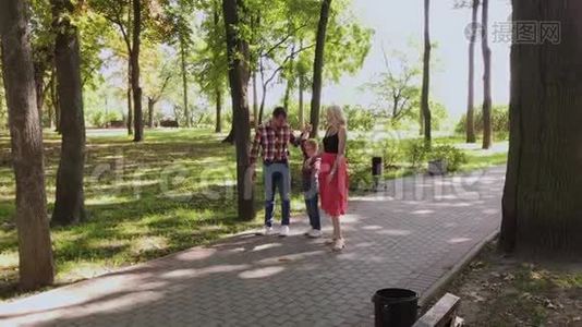 幸福的年轻一家沿着小巷在公园里散步。视频