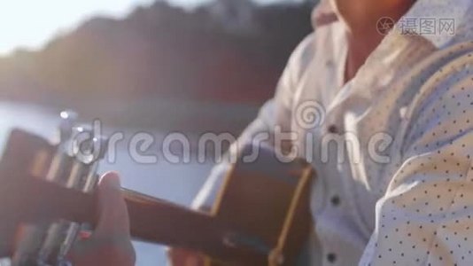 人弹吉他，对着湖面唱歌.. 吉他手触摸吉他弦。 近距离射击。视频