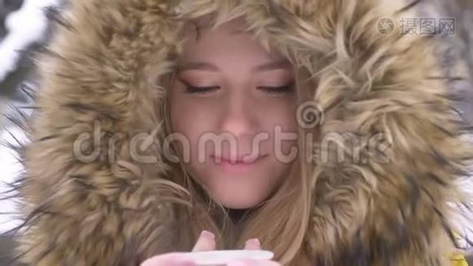 年轻的白种人女孩的特写照片，她喝着一杯热饮料，微笑着在冬天的街道上观看镜头视频