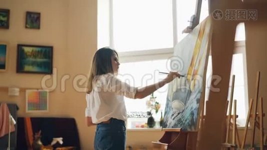忙碌的年轻女人是休闲服装，是用油画颜料站在画架附近，拿着画笔和调色板。 霍比特人视频