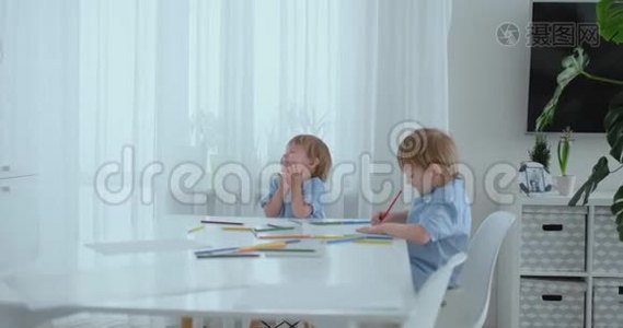 两个男孩兄弟坐在客厅的一张桌子旁，用铅笔在纸上画画。 妈妈过来拥抱孩子们视频