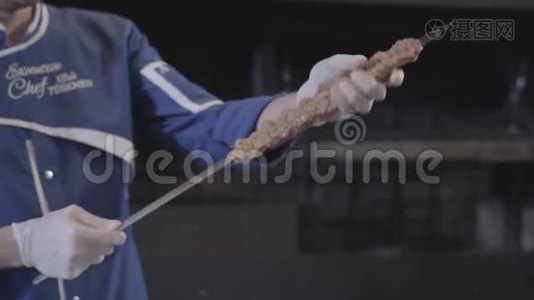 穿着蓝色厨师制服的熟练男子将肉串在扦子上，在现代餐厅形成卢拉串。 大型烤炉视频