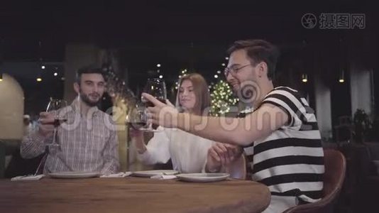 两个男人和女人坐在现代土耳其餐馆的桌子旁，用红酒叮叮当当地眨着眼睛。 朋友们视频