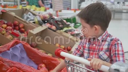 有趣的小男孩在超市的家庭购物中，坐在手推车里的盒子里摘苹果视频