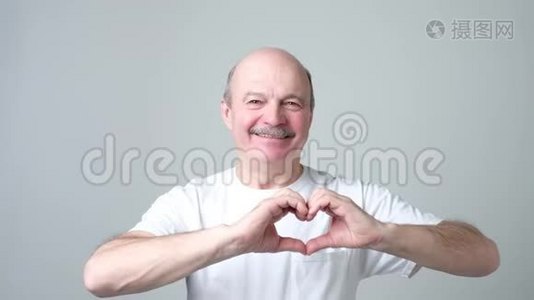 老人用手指微笑着看着相机，做着心形的爱标志。视频