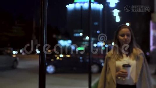 迷人的女孩带着咖啡，晚上沿着马路穿过城市。视频