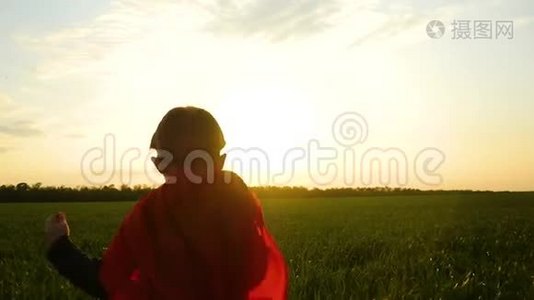 一个穿着超级英雄服装的孩子在夕阳的背景下穿过绿草视频