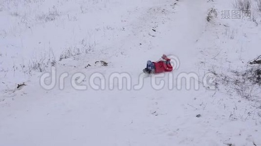 快乐的女孩在冬天白雪皑皑的雪橇上从雪山上滚下来，微笑着。 圣诞节假期。 慢动作视频