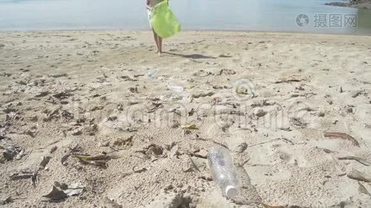 小女孩在沙滩上收集垃圾成绿色塑料袋，塑料瓶在海滩上收集。视频