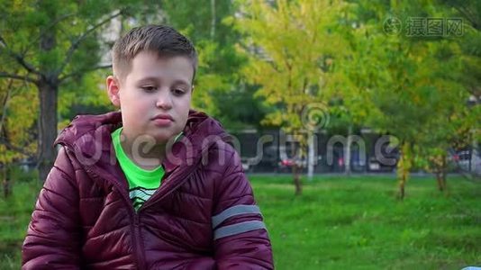 一个悲伤男孩的肖像。 坐在公园里，他`迷路了。视频