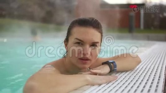 冬天，在炎热的室外游泳池边缘附近，美丽的黑发美女的亲密肖像。 蒸汽从水中升起，女孩视频
