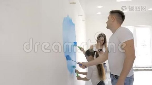 年轻的家庭在母亲查看短信时用滚筒粉刷墙壁视频