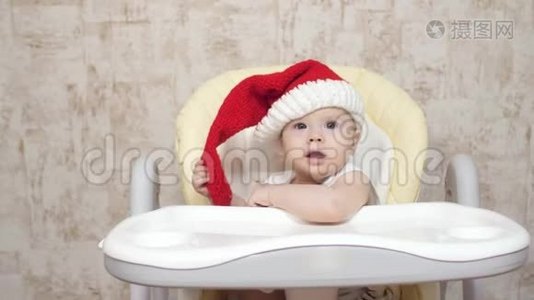 戴着红色圣诞帽的婴儿坐在高椅子上笑着。 圣诞节。 新年视频