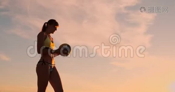 一位身穿比基尼、日落时带球的美女正准备在沙滩排球比赛中发球跳跃视频