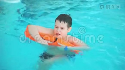 少年在游泳池里游泳，紧紧抓住橙色的花车。视频