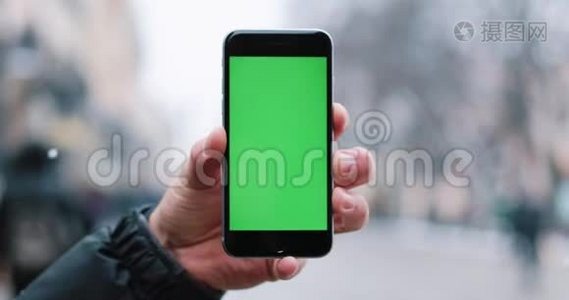 雪落在一个男人身上`他手里拿着智能手机，手里拿着绿色的屏幕视频
