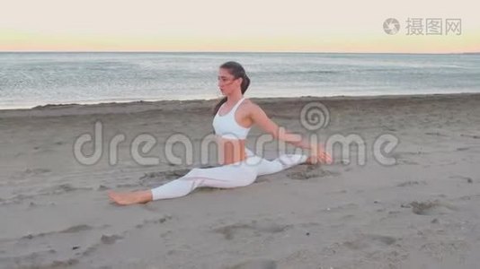日出时，年轻女子坐在沙滩上做瑜伽。视频