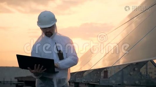 环保能源理念。男性太阳能建设者站在太阳能电池板附近操作笔记本电脑。视频