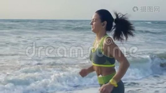 慢动作，耳机里的美丽女人在海边奔跑，引领健康的生活方式视频