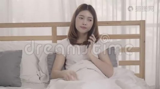 年轻的亚洲女人在早上醒来后躺在床上使用智能手机。视频
