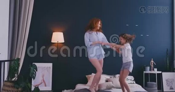 漂亮的妈妈和女儿在家里跳床时玩得很开心视频