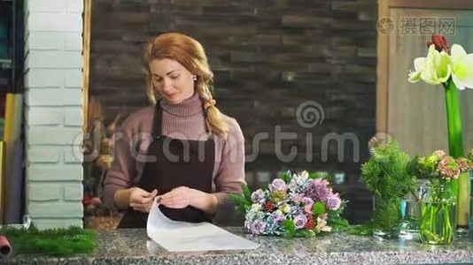 一个穿着围裙的女花店站在花店的柜台上，包着一束花。视频