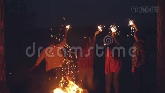 慢动作的后视图年轻男女游客站在森林里，手里拿着燃烧的火花，手在移动视频