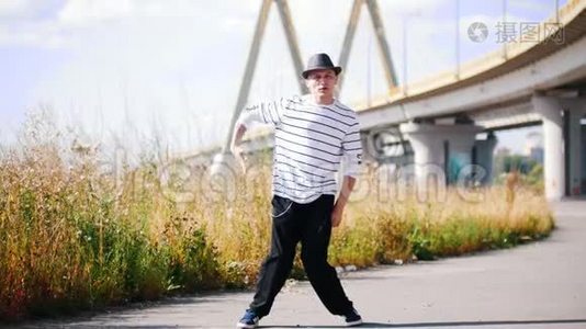 在炎热的夏日里，戴着帽子、穿着条纹T恤的街头舞蹈演员正聚精会神地在桥上跳着舞视频