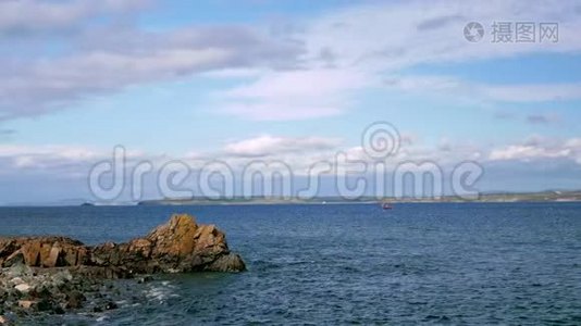 一艘小帆船在海里漂浮。 远处可见岩石海岸.视频