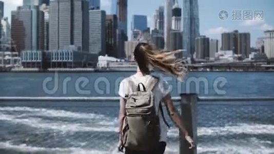 镜头跟随年轻快乐的旅行女孩背着背包，在纽约曼哈顿天际线上张开双臂跳跃。视频